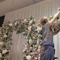 Person arranging a large floral arch with pink and white flowers