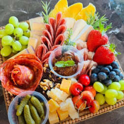 Charcuterie board with grapes, strawberries, cheese, salami, and pickles