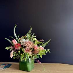 Pink and white mixed flower arrangement in a green glass vase