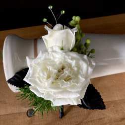 White rose boutonniere with green accents on a white holder