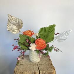 Orange roses in a white textured vase with fan-shaped leaves and metallic accents