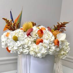 White floral arrangement with orange accents in a round white box