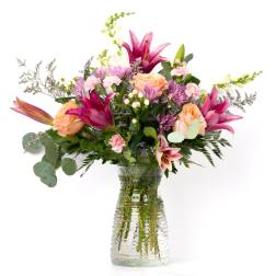 Mixed bouquet of pink lilies, peach roses, and pastel blooms in a clear textured glass vase