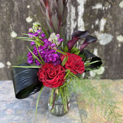 Bouquet of red roses, purple flowers, and dark calla lilies in a glass vase
