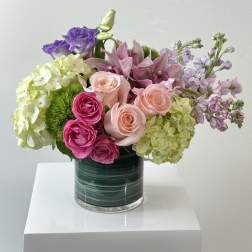 Mixed pink, purple, and green flowers arranged in a glass vase.
