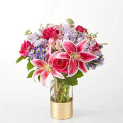 Pink lilies and roses in a clear vase with a gold base