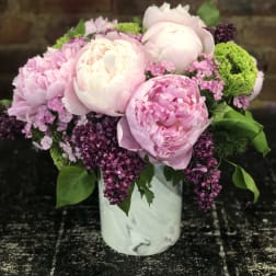 Pink peonies and purple blooms arranged in a white vase