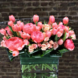 Pink tulips and small roses arranged in a clear glass vase