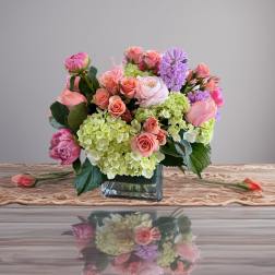 Pink and lavender flowers arranged in a square glass vase