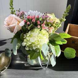 Bouquet of pale roses, hydrangea, and pink berries in a glass vase