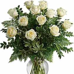 White roses arranged in a clear glass vase with lush greenery