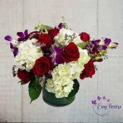 Red roses and white hydrangeas in a green glass vase with purple orchids