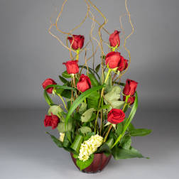 Tall arrangement of red roses in a burgundy vase with curly branches