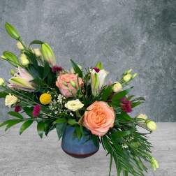 Mixed bouquet with peach roses and lilies in a blue vase
