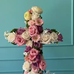 Cross-shaped floral arrangement of roses and pink blooms on a stand