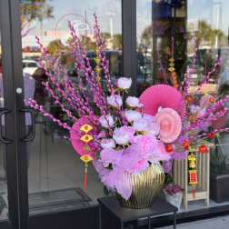 Pink floral arrangement in a gold vase with decorative fans and hanging ornaments