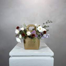 Mixed bouquet in a brown paper gift bag on a white pedestal