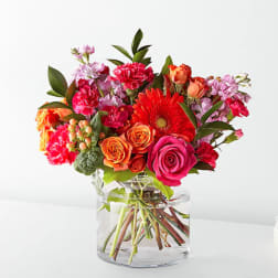 Bright mixed bouquet of roses, gerbera daisies, and carnations in a clear glass vase