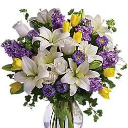Bouquet of white lilies, purple flowers, and yellow tulips in a glass vase