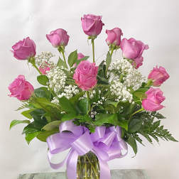 Pink roses in a glass vase with white baby's breath and a lavender ribbon