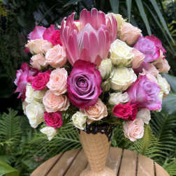 Pink and white roses arranged in a tall vase with a large pink protea