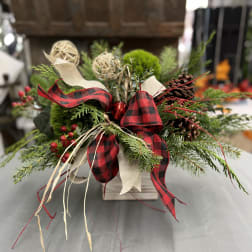 Holiday arrangement of evergreen branches with red plaid ribbon in a wooden container