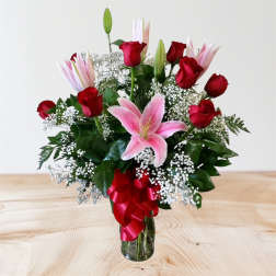 Bouquet of red roses and pink lilies in a glass vase with a red ribbon