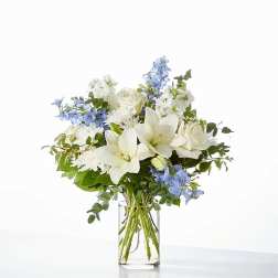 White lilies and roses with blue flowers in a clear glass vase