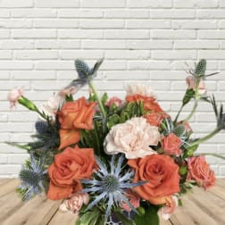 Orange and blush roses with blue thistle in a low bouquet