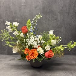 Mixed floral arrangement in a dark bowl vase with orange and white roses