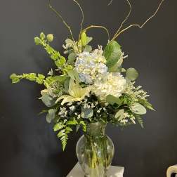 Tall white and pale blue floral arrangement in a glass vase