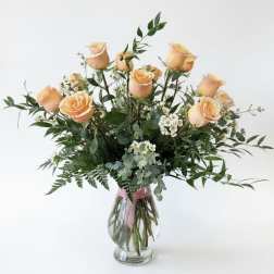 Peach roses in a clear glass vase with mixed greenery