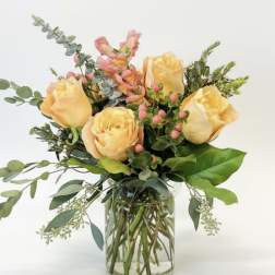Peach roses arranged in a clear glass vase with mixed greenery