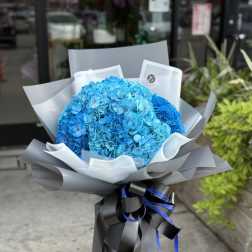 Bright blue hydrangea bouquet wrapped in gray paper with black ribbon