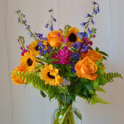Bouquet of orange roses, sunflowers, and blue flowers in a glass vase