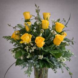 Yellow roses arranged in a clear glass vase with greenery