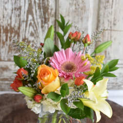 Mixed bouquet with roses, a pink gerbera daisy, lilies, and a glass vase