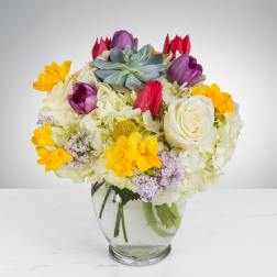Colorful bouquet with roses, tulips, hydrangeas, and a succulent in a glass vase