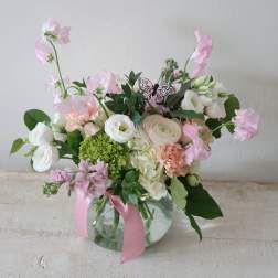 Pink and white flower arrangement in a glass vase with a pink ribbon