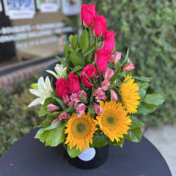 Bouquet of hot pink roses, yellow sunflowers, and white lilies in a black vase