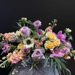 Mixed bouquet of pastel roses, tulips, and anemones in a low vase