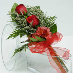 Red roses and pink flowers with a red ribbon in a clear vase