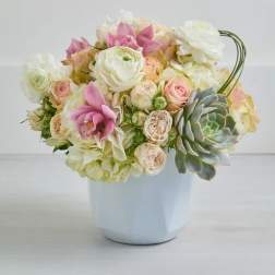 Pastel bouquet of roses, ranunculus, and orchids in a white vase