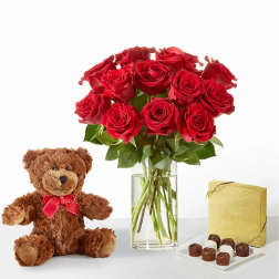 Red roses in a glass vase with a teddy bear and chocolates