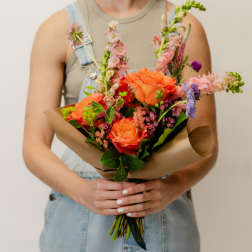 Person holding a colorful mixed bouquet wrapped in brown paper