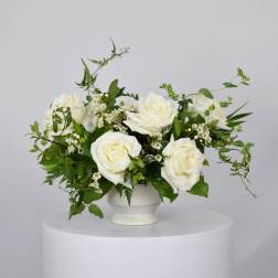 White roses arranged in a white vase with greenery