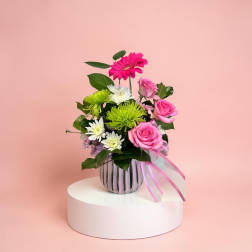 Pink and white flowers in a striped vase with a ribbon
