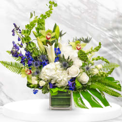 Mixed bouquet in a square glass vase with white, green, and blue flowers