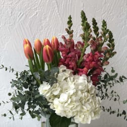 Bouquet of pink tulips, white hydrangeas, and magenta snapdragons in a glass vase