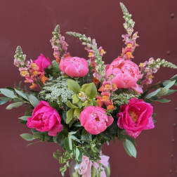 Pink peonies and snapdragons arranged in a glass vase with a pink ribbon